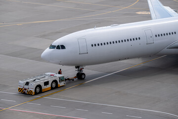 The apron transporter tows a modern narrow-body white passenger aircraft across the airfield of an...