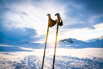 Sunset over a snowy winter mountain wilderness with ski poles standing in the deep snow.