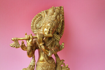 Lord Krishna is a golden sculpture on a pink background with space for text.