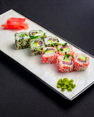 Sushi set, sushi rolls with cream cheese and caviar served on a white plate over black background.