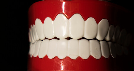 A smiling toy prosthesis, with white teeth and large eyes isolated against a black background.