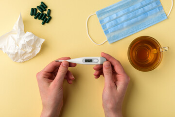 Hands holding a electronic thermometer with normal temperature on the display on yellow background...