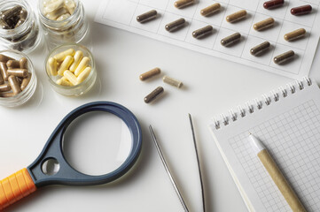 Medical capsules, magnifier and tweezers on the table in the pharmaceutical laboratory