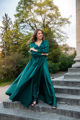 Naklejka premium full length young elegant woman in beautiful green gress standing in stone stair