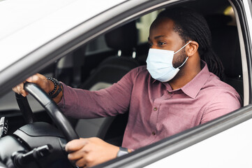 African American male taxi car driver wearing protective face mask or respirator for protection against viral diseases, sitting at the front, behind the wheel. Healthcare, safety in pandemic concept