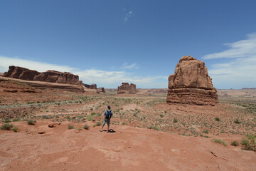 A hiker looking at the vast landscape and red sandstone formations at Arches National Park in Utah on a sunny day