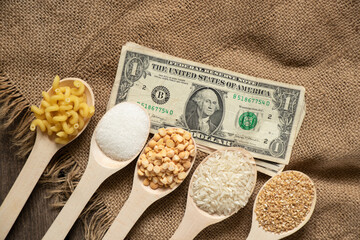 sugar rice peas pasta cereals on wooden spoons and american dollars on the table on the kitchen,...