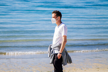 man with medical mask in protection of the coronavirus in the new normal walking on the beach