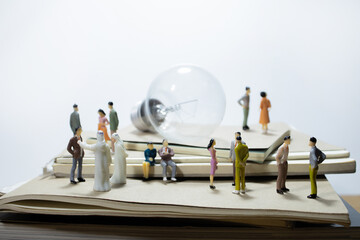 group of miniature business people meeting on pile of books with light bulb. 