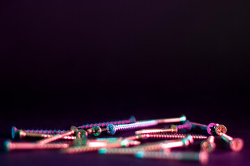 minimalist macro shot of a bunch of self-tapping screws on a black background in pink and blue neon light with shallow depth of field, copy space