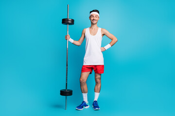 Full length photo of young skinny man happy positive proud exercise weightlifting isolated over blue color background