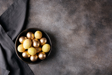 Dark plate with golden easter eggs on dark concrete background, flat lay, copy space, horizontal orientation
