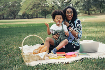 Happy picnic relax black people mom with son blowing bubbles in garden