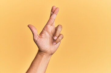 Arm and hand of caucasian man over yellow isolated background gesturing fingers crossed, superstition and lucky gesture, lucky and hope expression