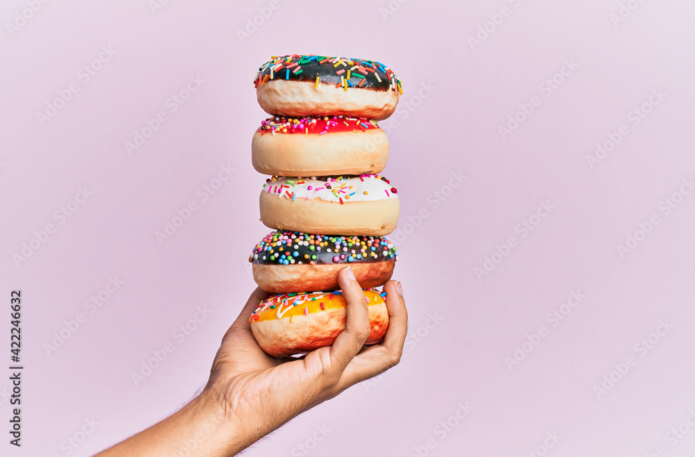 Wall mural Hand of hispanic man holding tower of donuts over isolated pink background.