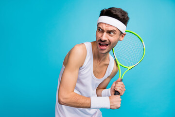 Photo of young sportive man hold tennis racket afraid scared look empty space isolated over blue color background