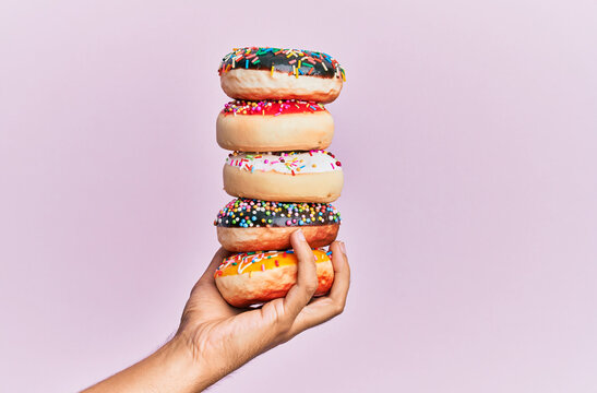 Hand of hispanic man holding tower of donuts over isolated pink background.