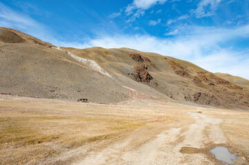 Scenic view over Akkol valley, surrounded by dry hills and mountains, stone formations, harsh environment on a sunny day with blue sky and clouds. Altai autumn landscape, Russia
