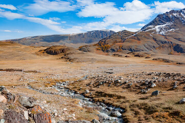 Scenic view over Akkol valley, surrounded by mountains, stone formations, harsh environment on a sunny day with blue sky and clouds. Altai autumn landscape, Russia