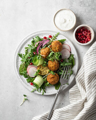 Falafel and fresh vegetables salad on a white ceramic plate on concrete background, top view. 