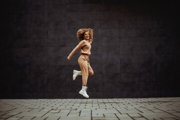 Full length of cheerful hip hop girl in tracksuit jumping in place.