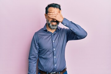 Obraz premium Middle age man with beard and grey hair wearing business clothes smiling and laughing with hand on face covering eyes for surprise. blind concept.