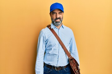 Middle age man with beard and grey hair wearing delivery courier cap winking looking at the camera...