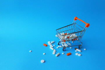 Tablets, capsules and a shopping cart on a blue background. The concept of buying drugs, prices for treatment. Sales in the pharmacy.