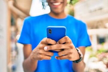 Young african american man smiling happy using smartphone at street of city.