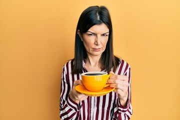 Young hispanic woman drinking a cup of coffee skeptic and nervous, frowning upset because of...