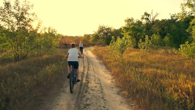 Happy family, mother and son in the park ride a bicycle along the path in the forest in the rays of beautiful sunset. A family of cyclists. Athletic family. A healthy lifestyle.