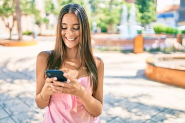 Young hispanic woman smiling happy using smartphone walking at the park