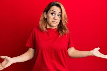 Hispanic young woman wearing casual red t shirt clueless and confused expression with arms and...