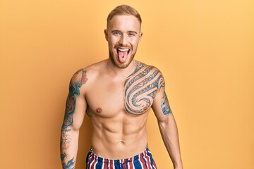 Fototapeta premium Young caucasian man wearing swimwear shirtless sticking tongue out happy with funny expression. emotion concept.