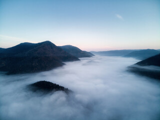 Aerial view, sea of fog and clouds illuminated by the rising sun, snow on the tops of the mountains. Russia