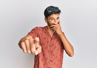 Young handsome man wearing casual summer clothes laughing at you, pointing finger to the camera with hand over mouth, shame expression