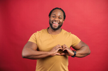 Romance concept. Smiled and handsome dark skinned man shows heart shape with hands, happy African...