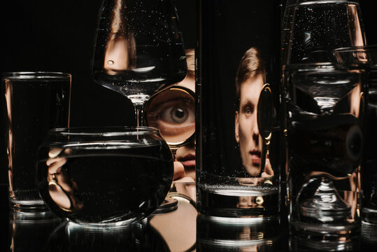 Fototapeta man looking through a magnifying glass and glasses of water with reflections and distortions