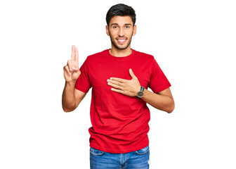Young handsome man wearing casual red tshirt smiling swearing with hand on chest and fingers up,...