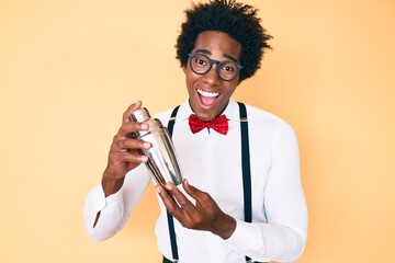 Handsome african american bartender man with afro hair preparing cocktail mixing drink with shaker smiling and laughing hard out loud because funny crazy joke.