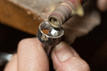 goldsmith sands a silver ring on the workbench.