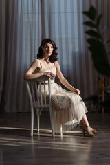 Fototapeta premium Cute young girl sitting in the studio on a beautiful vintage chair. The hand is on your knees.