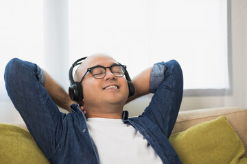 Young asian man wearing headphone and listen the music. He in living room sitting on sofa.