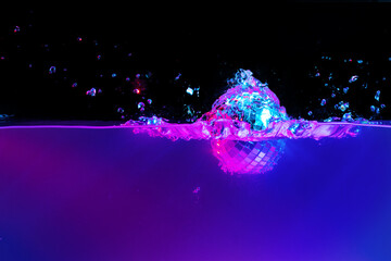 Disco ball falling into the water with a splash against black backgorund, neon light