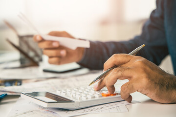Young man was using a calculator to calculate his income and expenses. In his hand there were bills to pay a lot in debt.