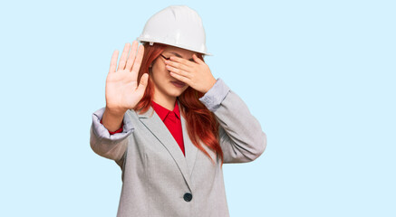 Young redhead woman wearing architect hardhat covering eyes with hands and doing stop gesture with sad and fear expression. embarrassed and negative concept.