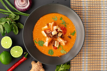 Tom yam Thai soup in black bowl served on gray background