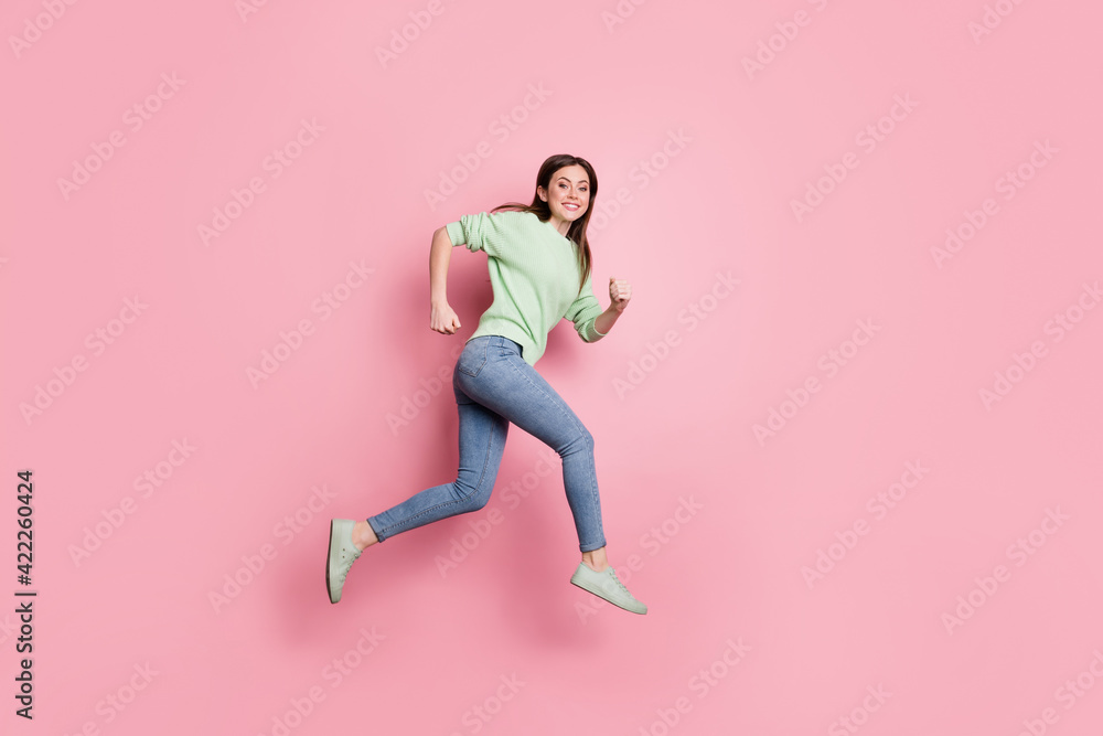 Poster Full size profile photo of brunette nice girl jump run wear lime sweater jeans sneakers isolated on pink color background