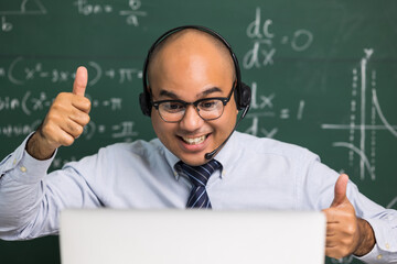 Indian young teacher man sitting wearing headset teaching online video conference live stream by laptop. Asian teacher teaching mathematics class webinar online for students learning.