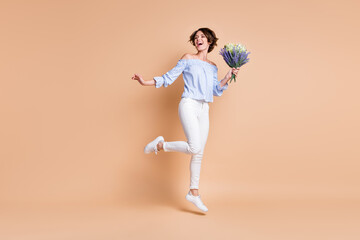 Fototapeta na wymiar Full length photo of young attractive cheerful girl happy hold bouquet jump look empty space isolated over beige color background